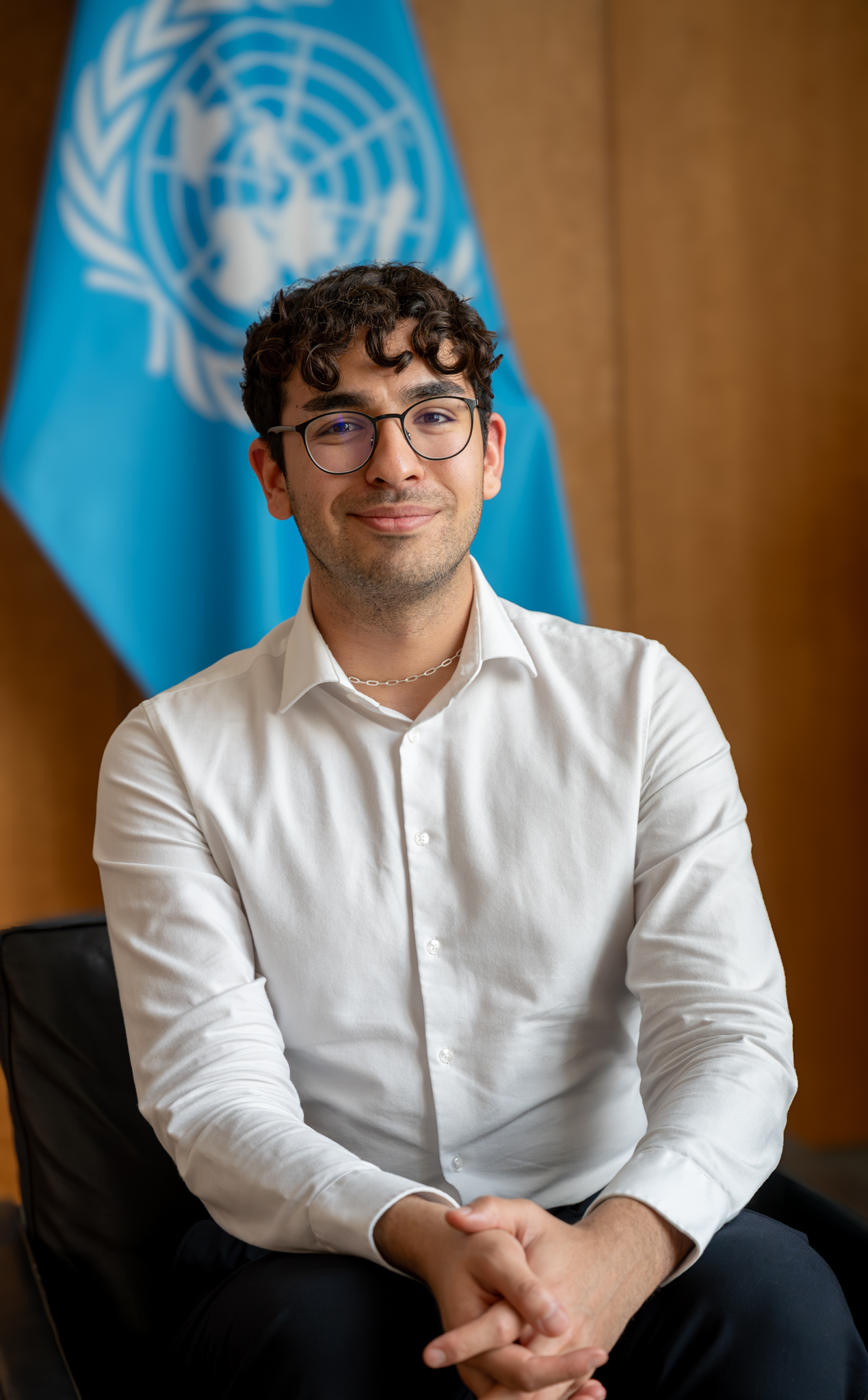 Portrait of Emirhan Dalci seated in front of a United Nations flag